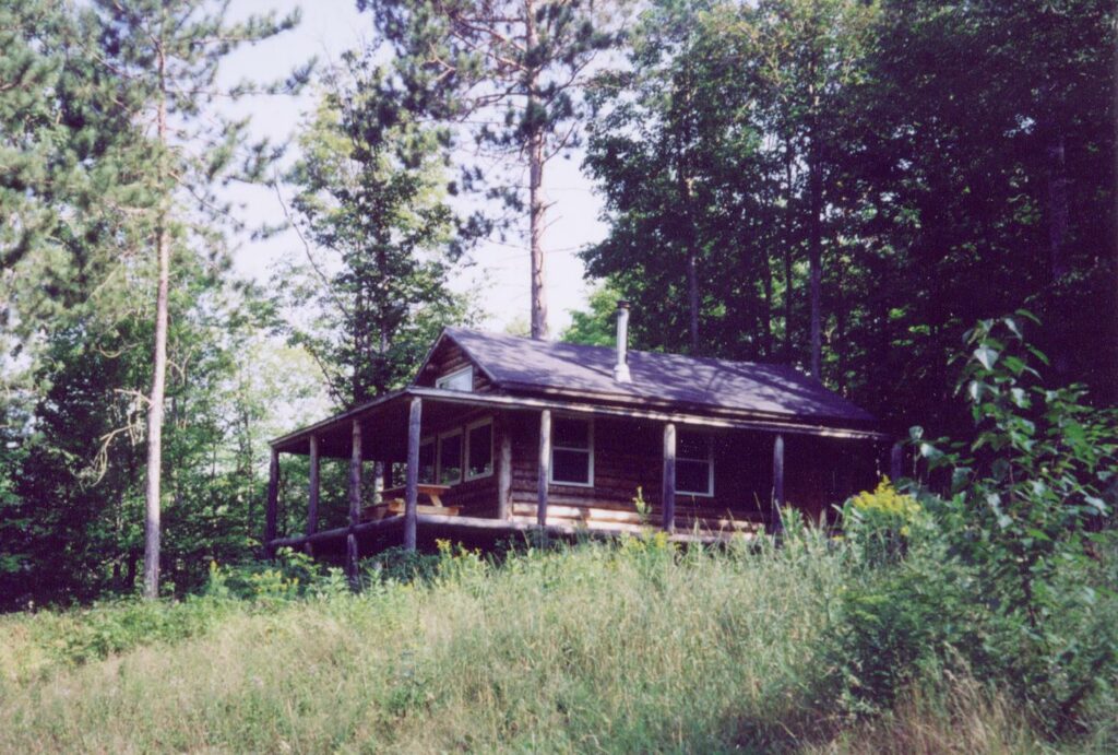 View of log cabin on a hill in a field, sheltered by trees