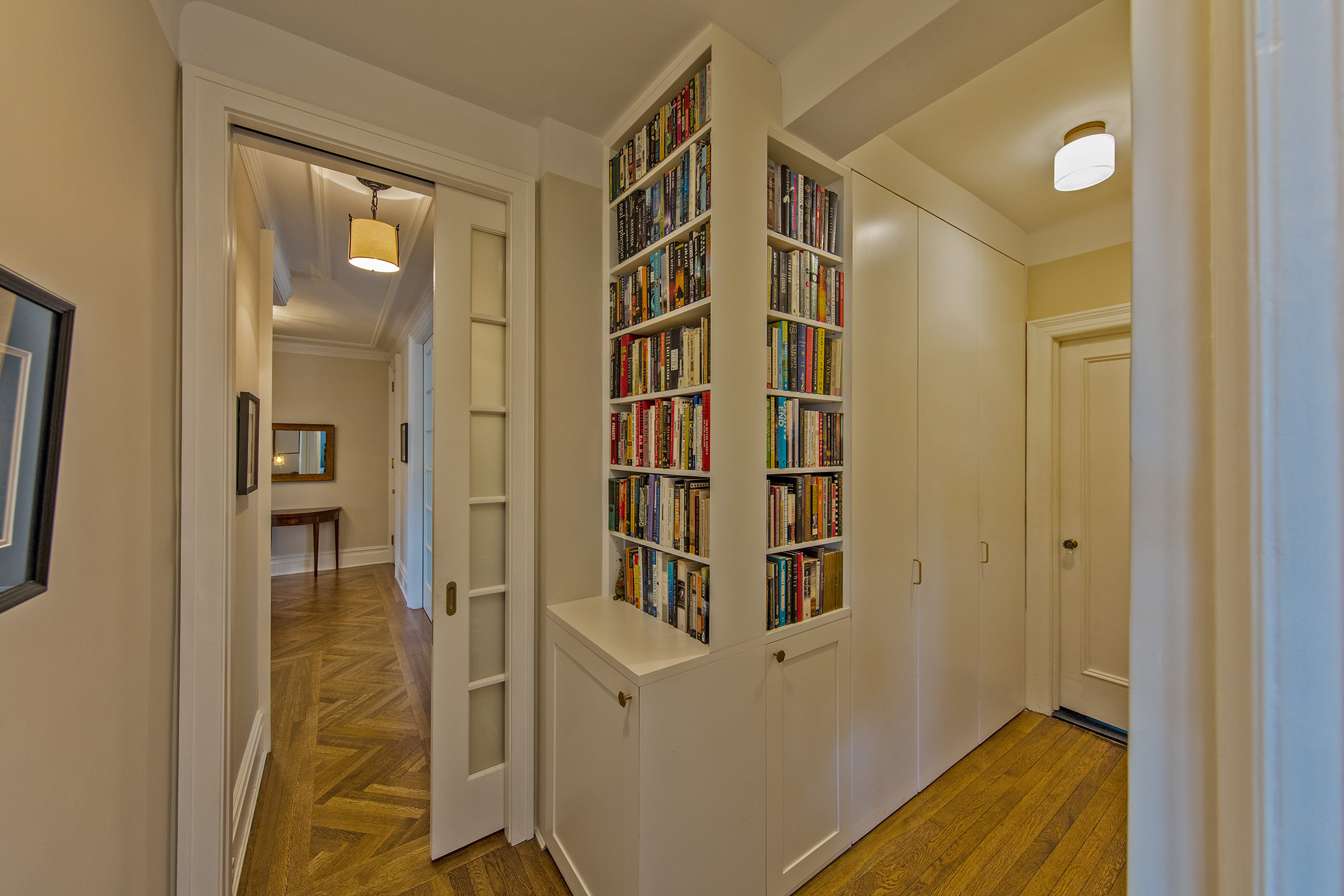 After: The corner has become a bookshelf above and storage below, the closet space is more accessible with double doors leading, to the left the doors to the Living room, Foyer, and Dining Room are visible.