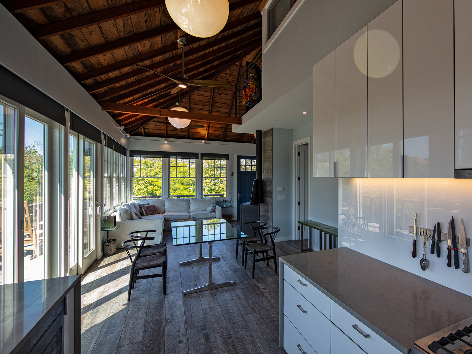 Kitchen After: A open plan 20’ long galley Kitchen connects with the Dining and Living areas. The dark wood rafters uncovered above balance the bright light from wall-to-wall double-hung windows stretching to the front of the house