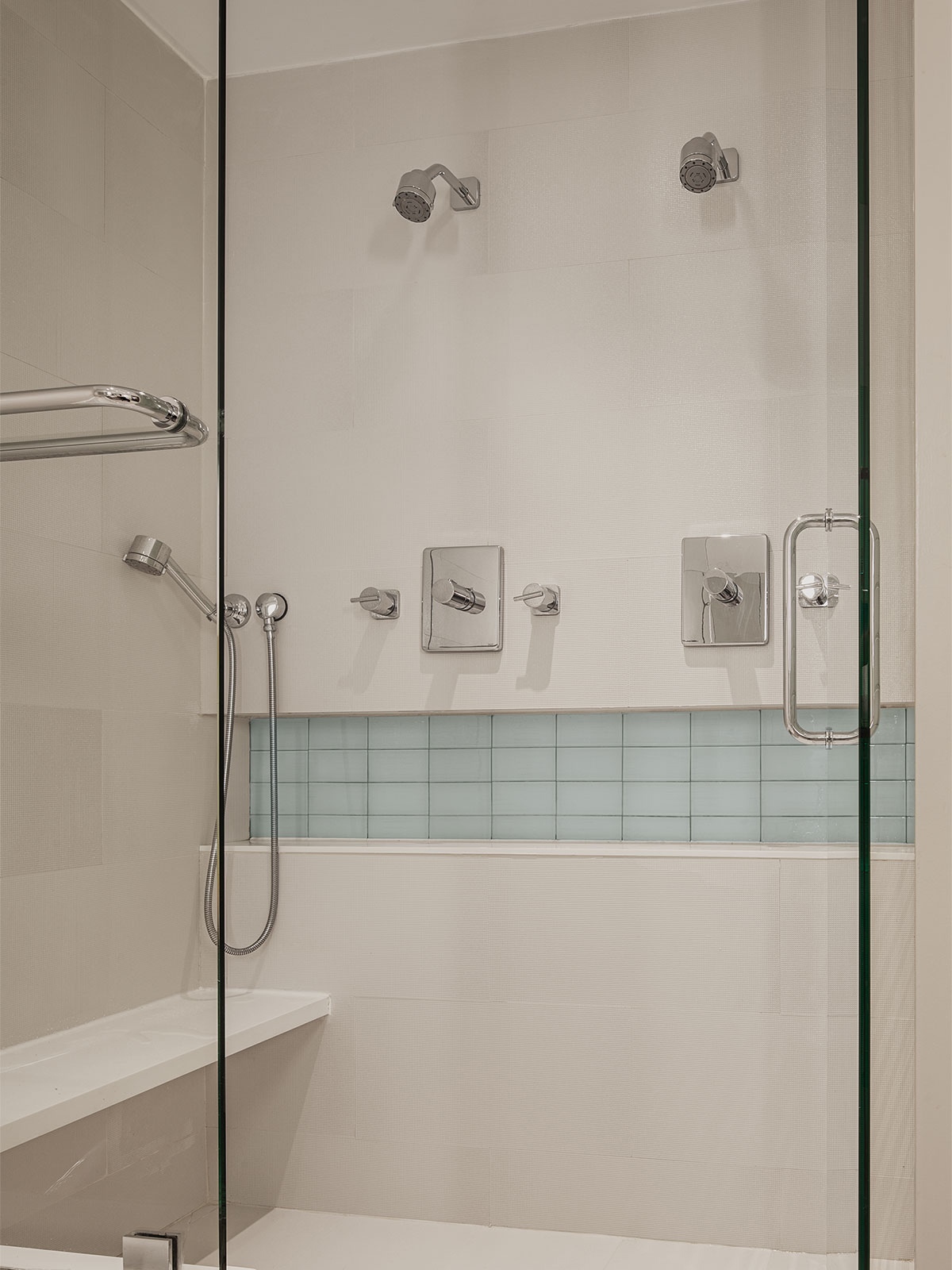 A textured white tile-clad double shower has a built-in bench on the left and a full-width niche for shower supplies with an accent of clear glass tile.
