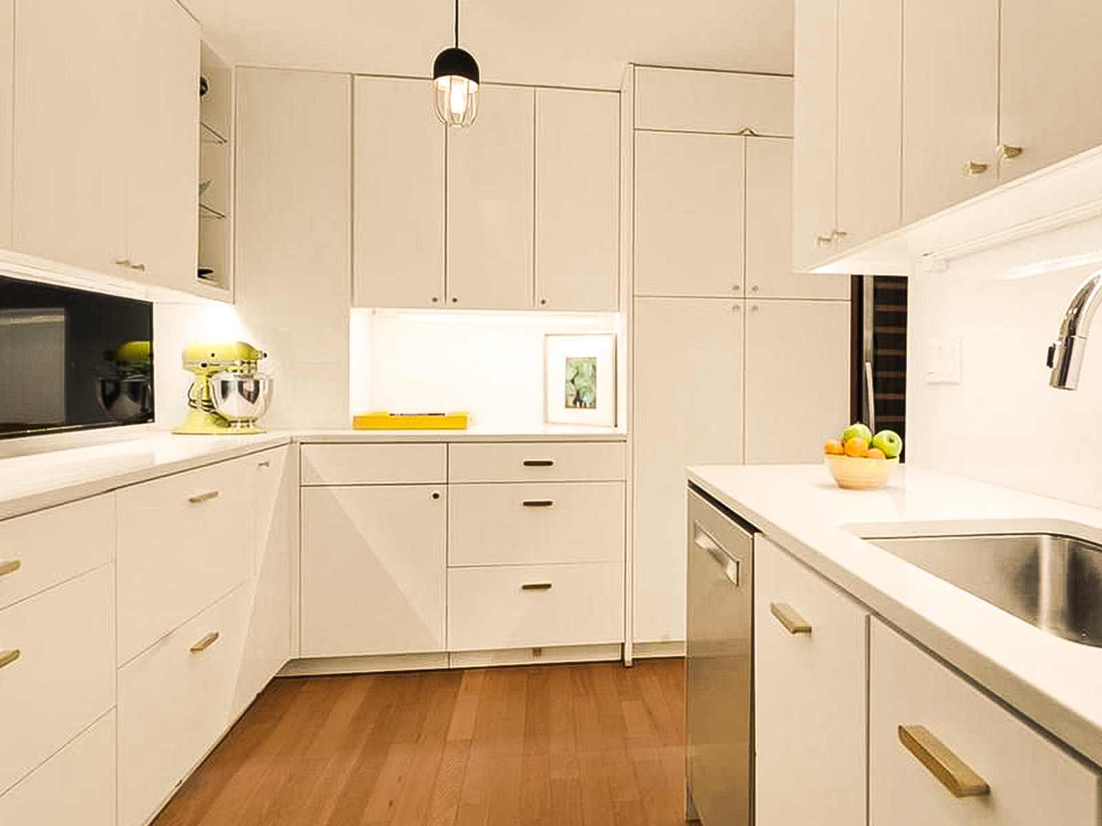 White cabinets with brightly-lit white countertops and warm wood floors