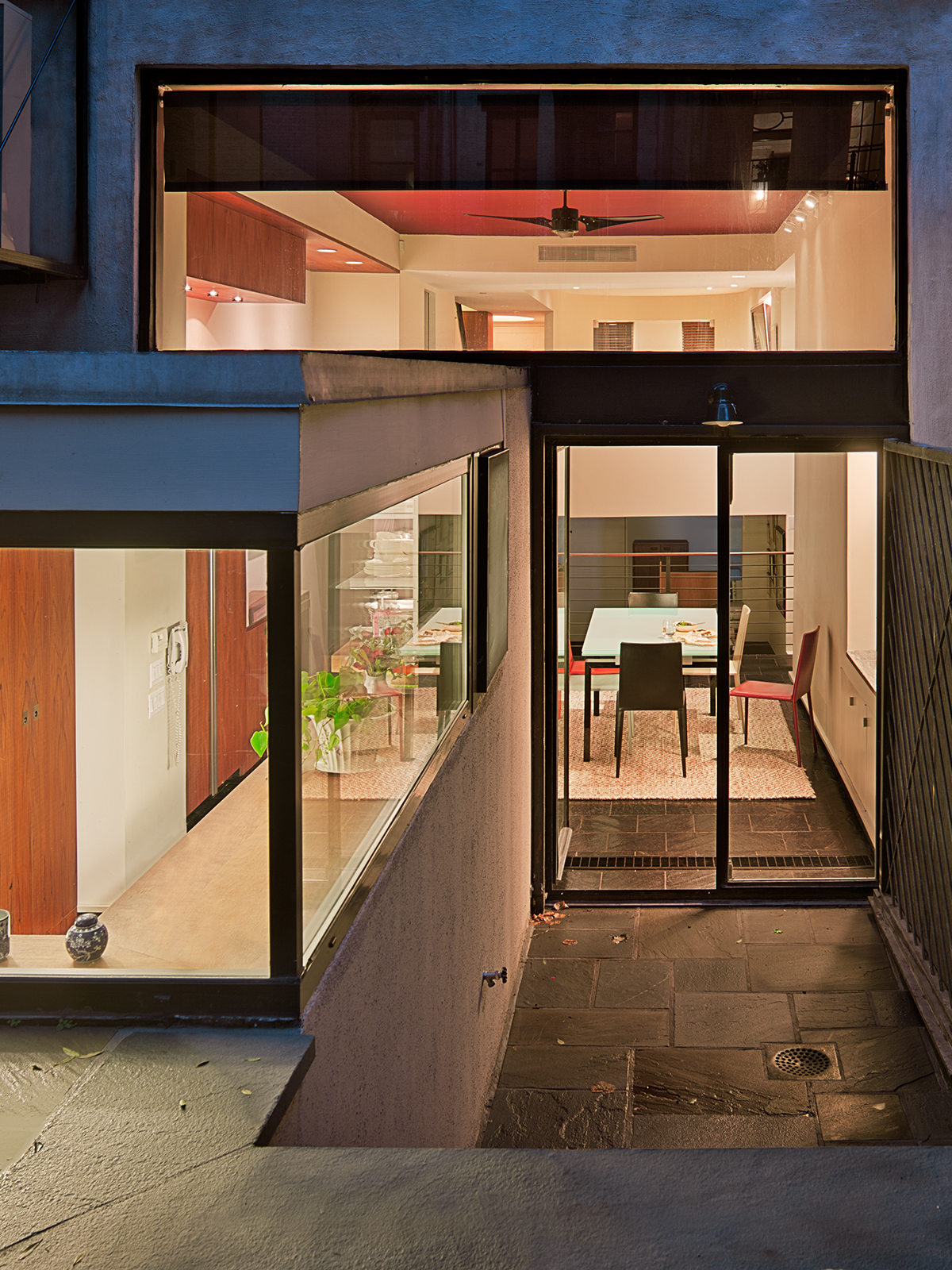 At dusk, the house glows; the galley Kitchen projects out from the double-height glass facade of the rear of the townhouse.