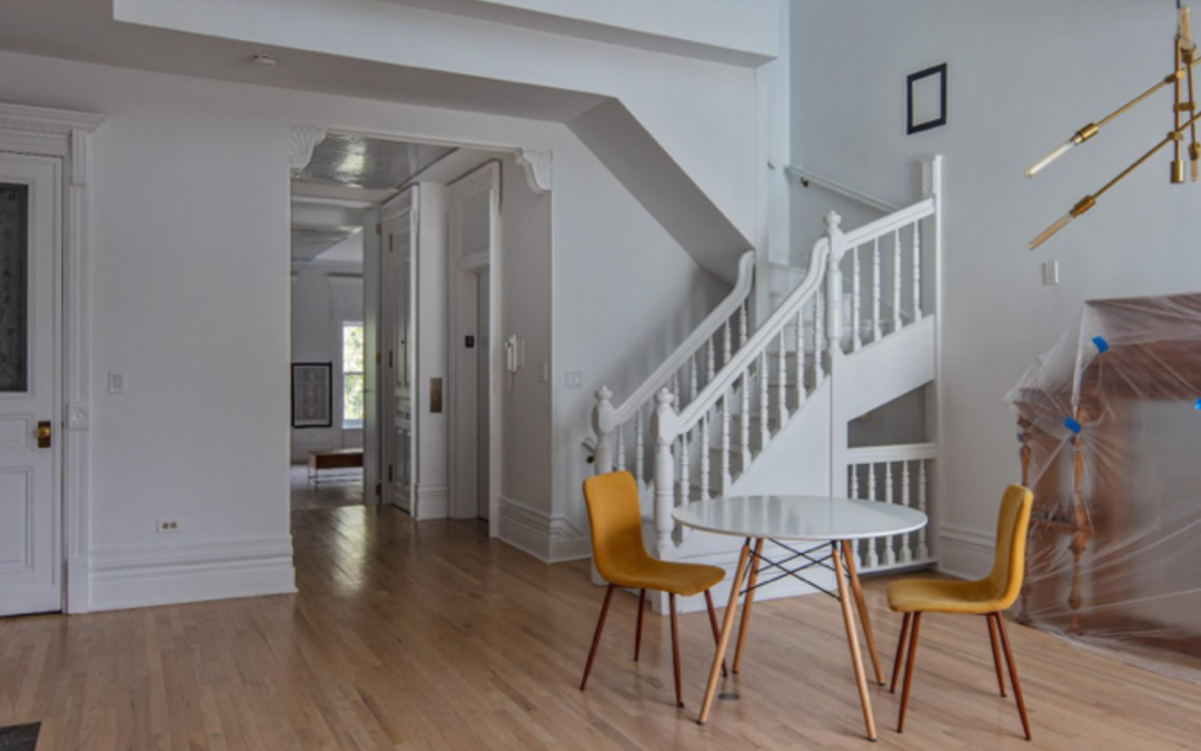 Large room with thin wood strip floors and a white painted Victorian staircase opens onto a small entry way, light filters from above