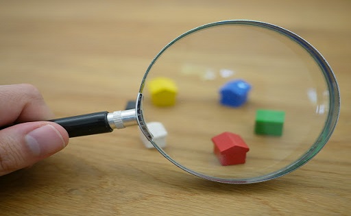 A magnifying glass examines miniature houses against a wooden background. 