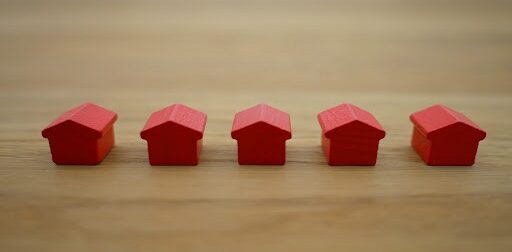 A row of five, red-colored miniature houses against a wooden backdrop.