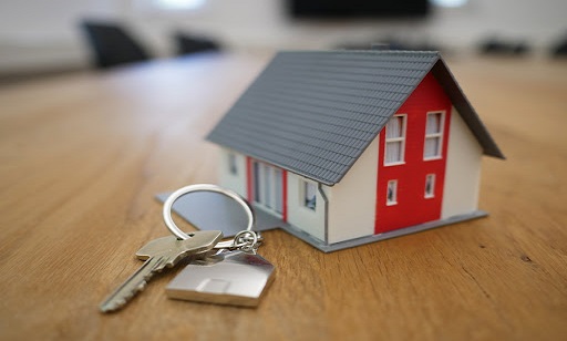 A miniature house and a set of keys against a wooden tabletop.