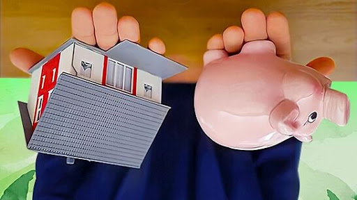 an upside down image of two hands holding a pink piggy bank on the right and a toy house on the left. A wood table-top hovers above, against a leafy green background.