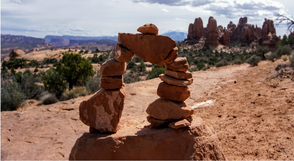 A doorway created but a stacked pile of small reddish rocks sitting on the side of a reddish dirt trail