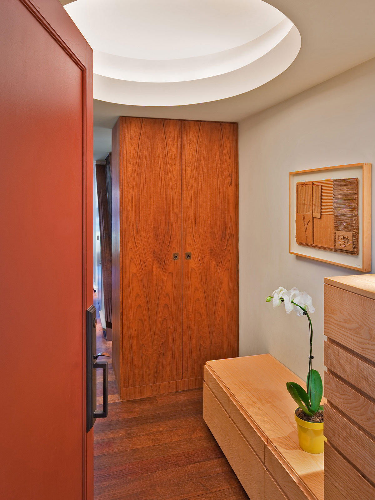 On the left, a red Entry door opens to a 5’ wide space with cabinets and floors of complementary wood species and a 48” x 54” glowing oval recessed light above.