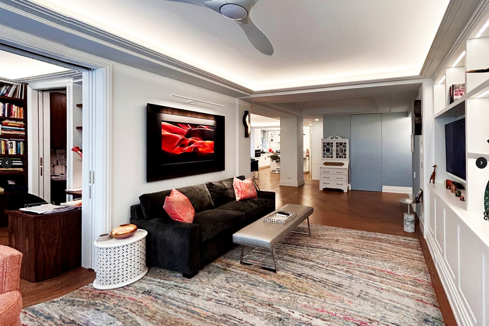 After: A spacious and light-filled furnished living room opens onto the foyer with views to the dining area and Kitchen beyond and the home office to the left. Cove lighting is used in all of the rooms that are visible to create a soft brightness.