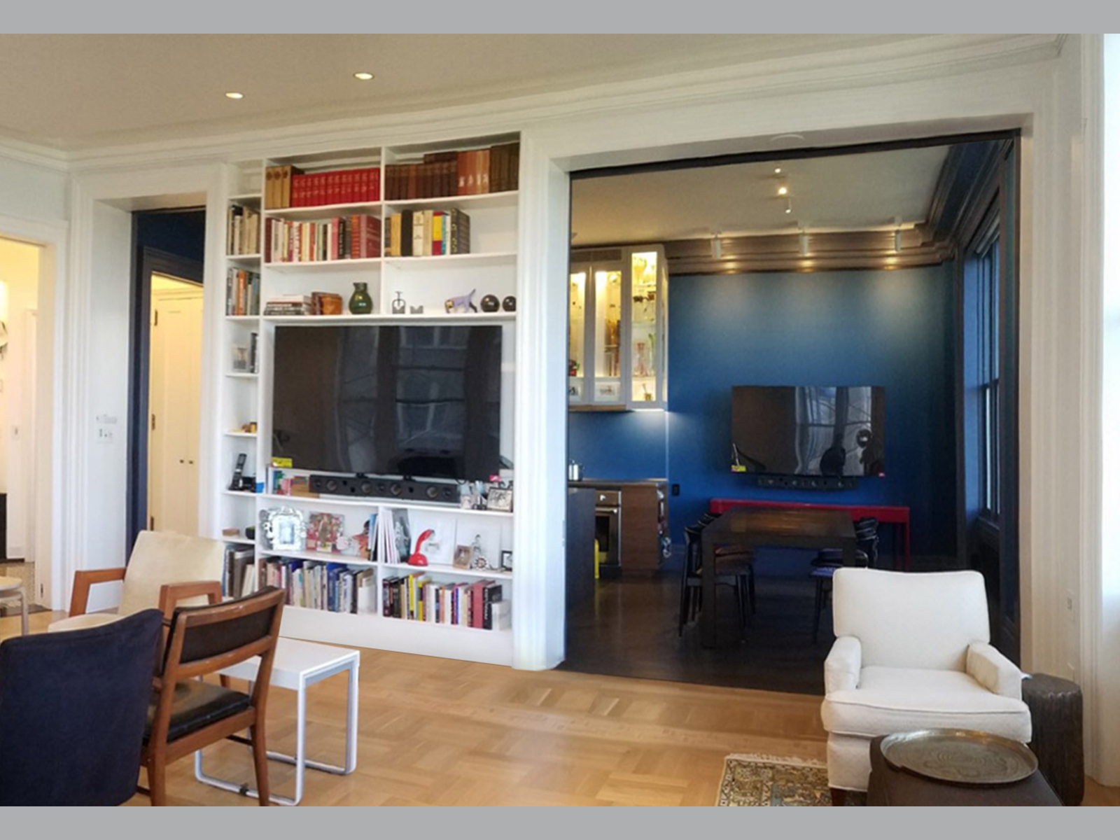 Living Room with two tall doors and one triple-wide tall door lead to Foyer and an Azure dining Room punctuated by a wall of books with a TV in it