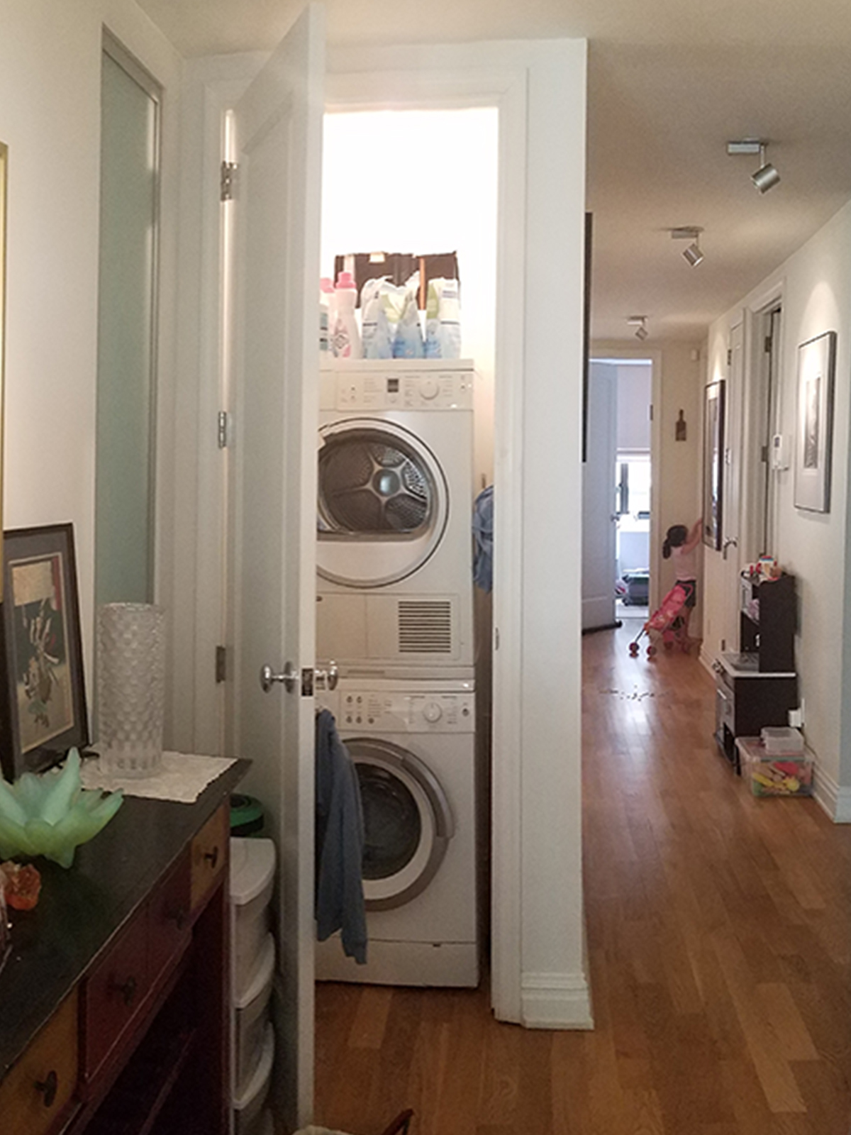 An open closet door reveals a stacking washer and dryer in a narrow corridor.