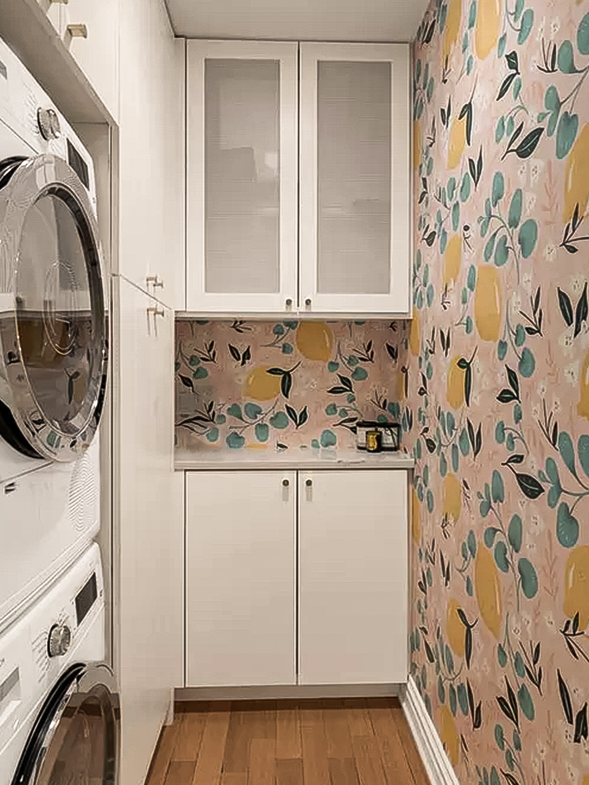 A narrow room: white lacquered linen cabinets surround a stacking washer/dryer with a countertop at the far end, a colorful