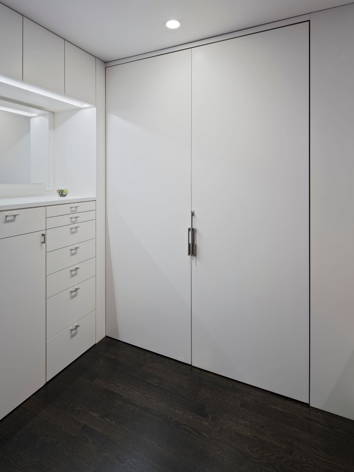 A floor-to-ceiling built-in closet with sizeable flat panel doors and a multi-drawer built-in dresser is set off against an almost-black floor.