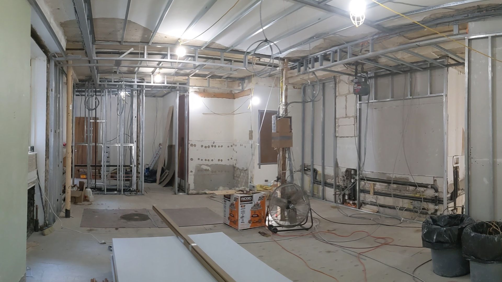 An interior space under construction with exposed metal studs, pipes, and electrical wires.